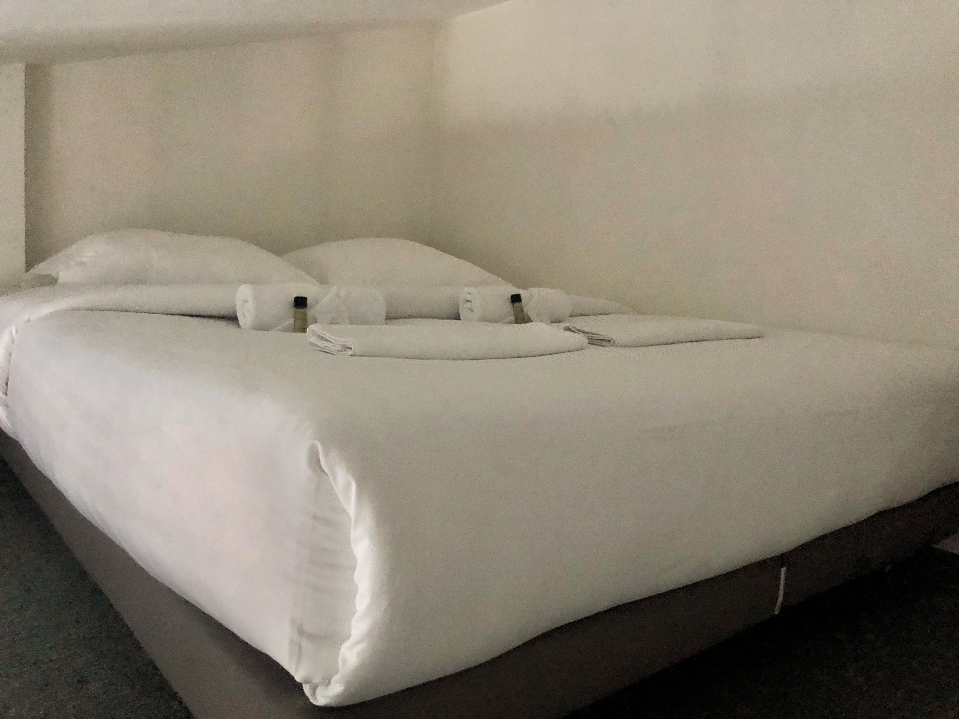 Un lit bien fait, avec du linge de lit blanc et des oreillers, une tête de lit sombre et une décoration simple et épurée.