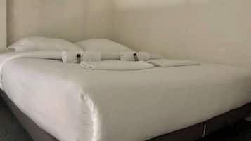 Un lit bien fait, avec du linge de lit blanc et des oreillers, une tête de lit sombre et une décoration simple et épurée.