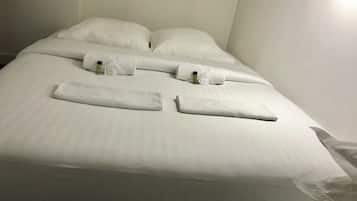 A neatly made bed with white linens and towels, a bottle of lotion, and a small toiletry bag.