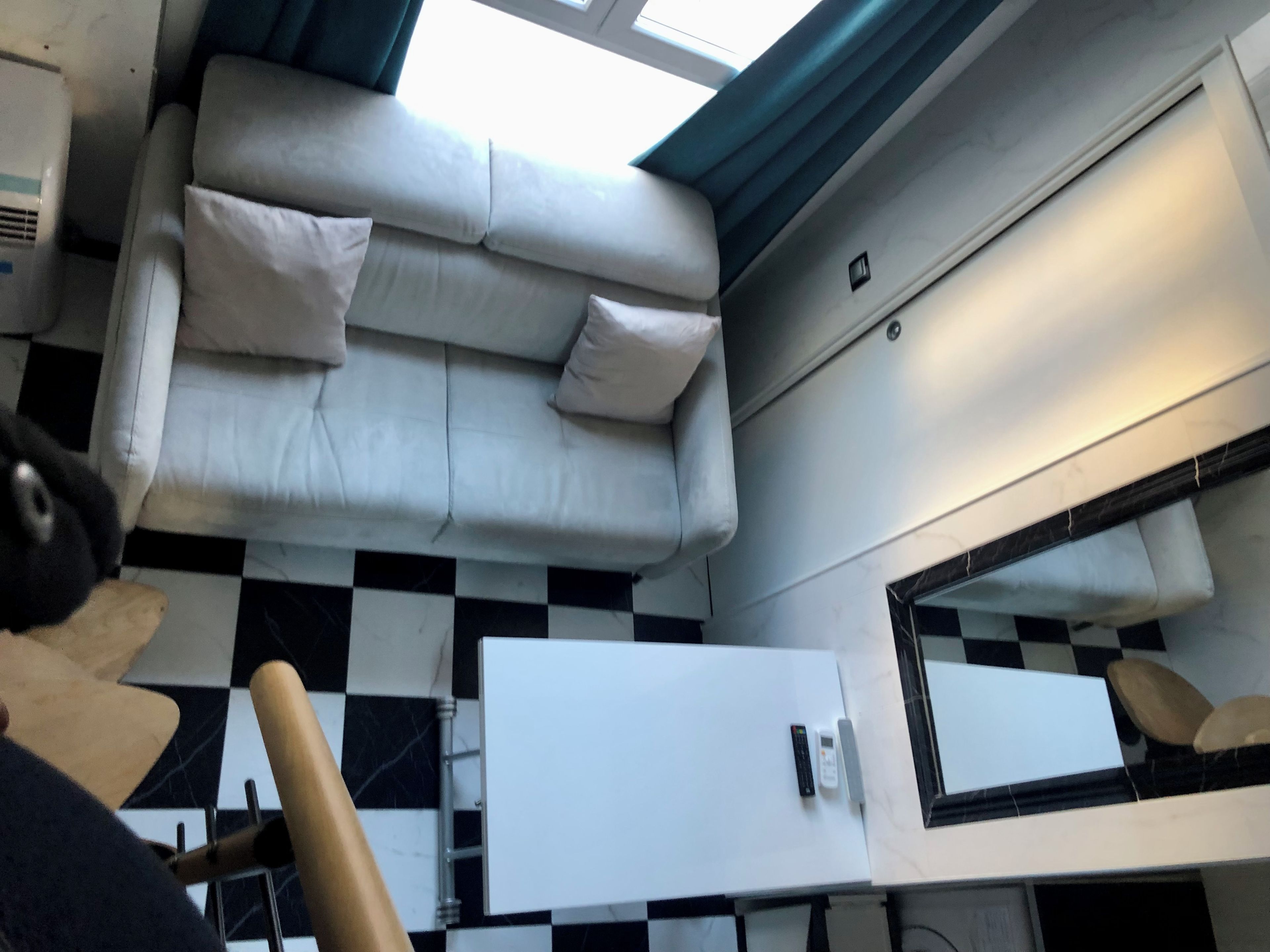 Une pièce avec un sol à carreaux, un canapé blanc avec des coussins, une armoire blanche et un miroir.