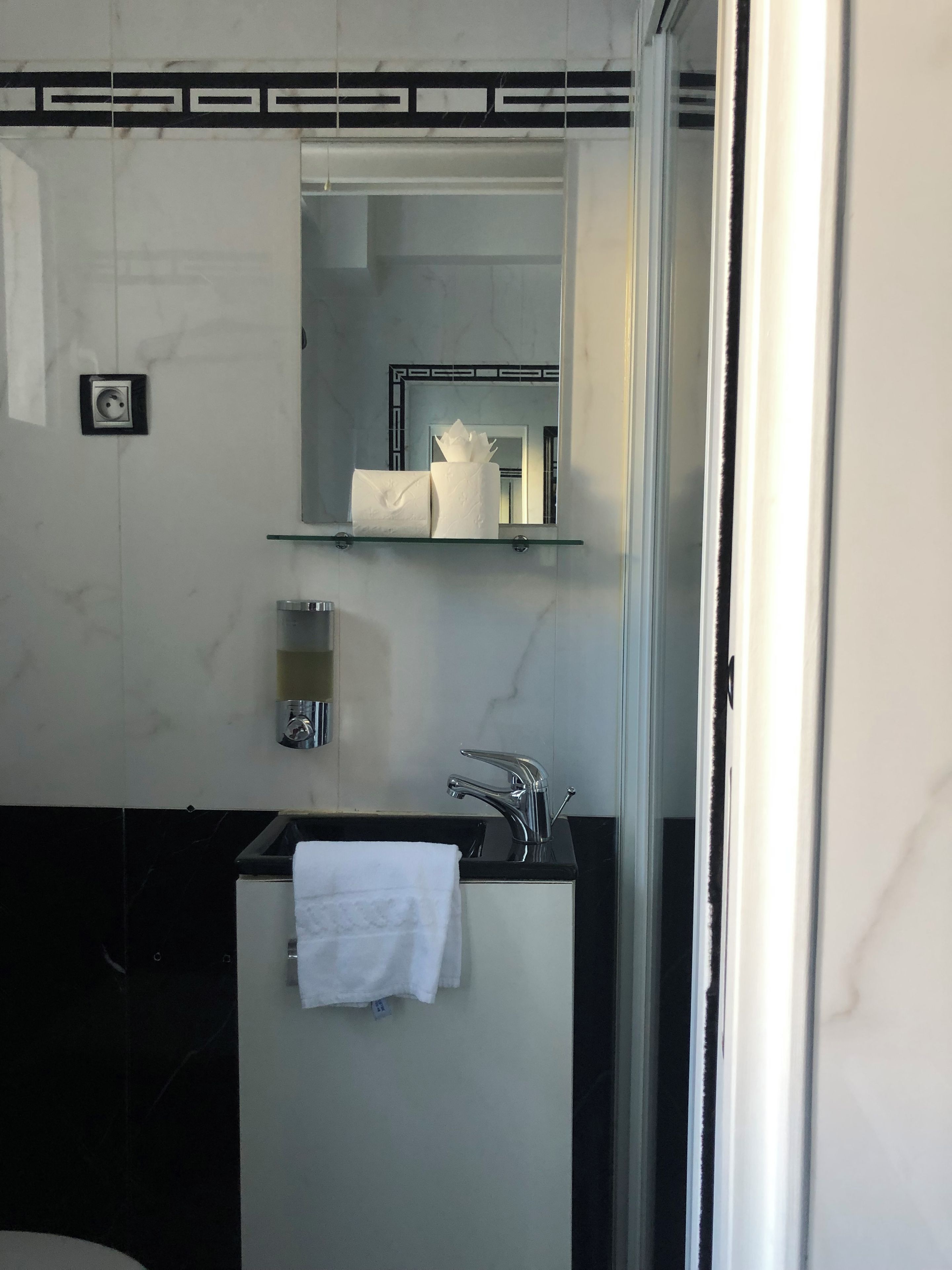 A bathroom with a mirror, a towel hanging on the wall, a sink, and a shelf with toiletries.