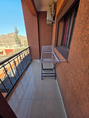 A balcony with a metal drying rack, a window with a red curtain, and a view of a hilly landscape. - Lady Plaza Apartment (Marrakech)