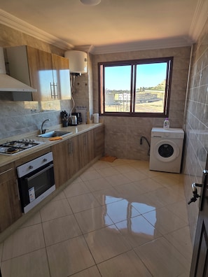 A kitchen with a gas stove, oven, sink, and a window with a view of buildings. - Lady Plaza Apartment (Marrakech)