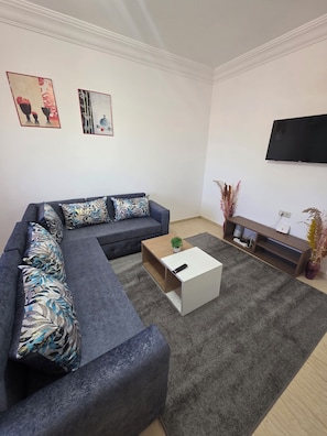A modern living room with a sectional sofa, a coffee table, a flat-screen TV, and artwork on the wall. - Lady Plaza Apartment (Marrakech)