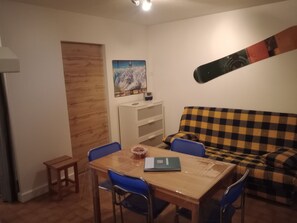 A room with a dining table, chairs, a sofa, and a wall-mounted snowboard. - Mountain studio apartment with sleeping alcove for 4 people in Saint-Lary-Soulan, renovated in 2026. (Saint-Lary-Soulan)