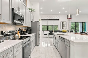 A modern kitchen with stainless steel appliances, a central island, and a dining area with a view. - Luxury 15br Suites Pool and Themed Bedrooms (Orlando)