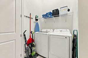 A laundry room with two washing machines, a red vacuum cleaner, and a laundry basket on a shelf. - Luxury 15br Suites Pool and Themed Bedrooms (Orlando)