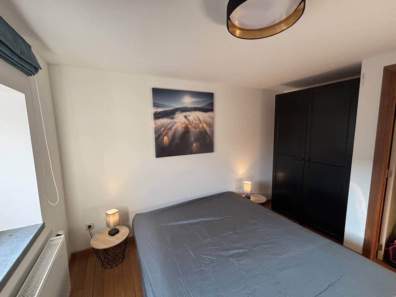 A bedroom with a bed, bedside lamps, a wall-mounted picture, and a wardrobe.