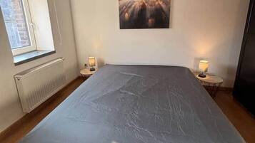 A bedroom with a large bed, a window, a radiator, a wall-mounted picture, and two bedside lamps.