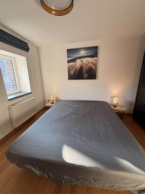 Ein Schlafzimmer mit einem großen Bett, einem Fenster, einem Heizkörper, einem Wandbild und zwei Nachttischlampen.