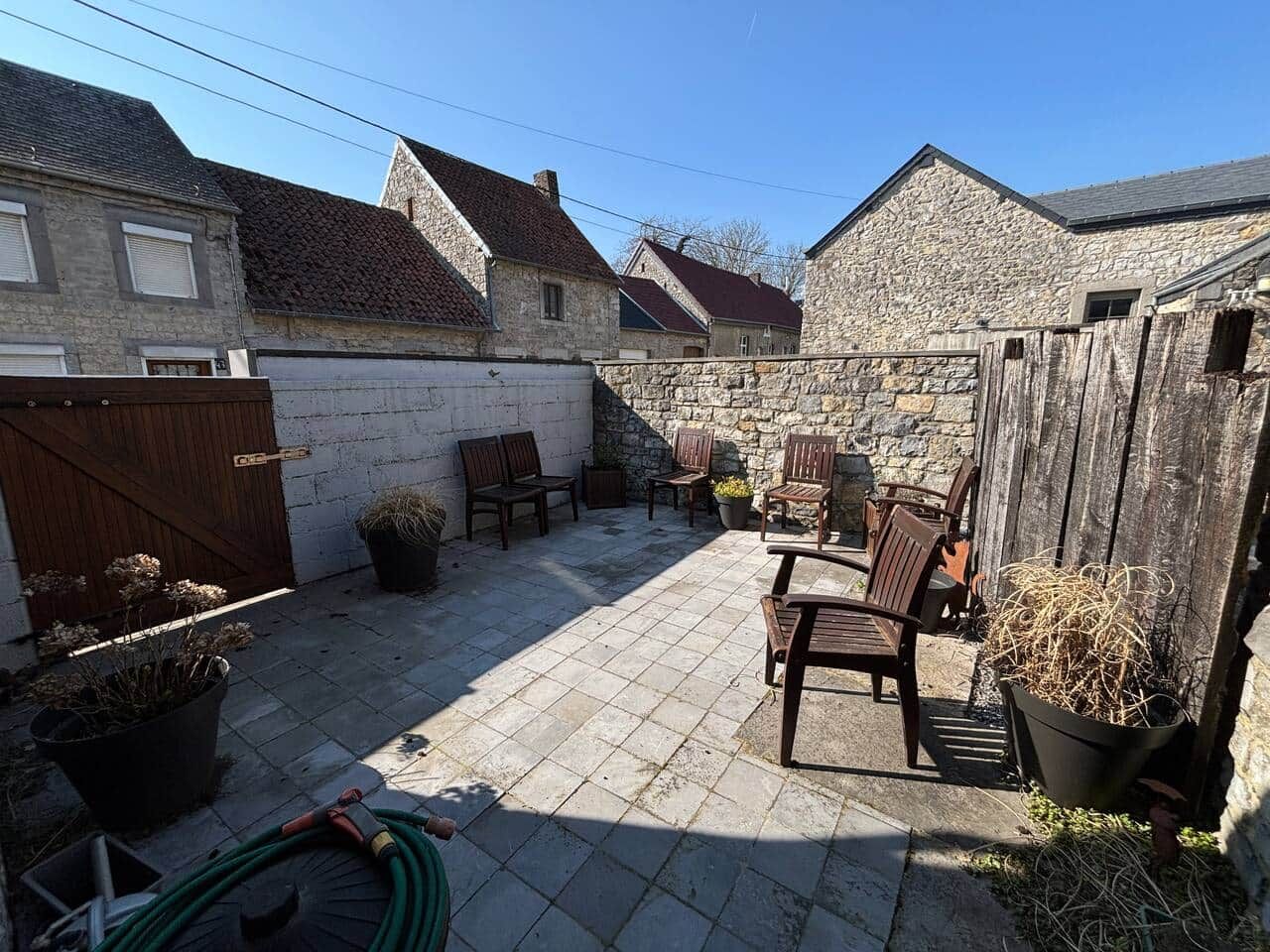 Un patio con suelo de piedra, mobiliario de madera y plantas en macetas.