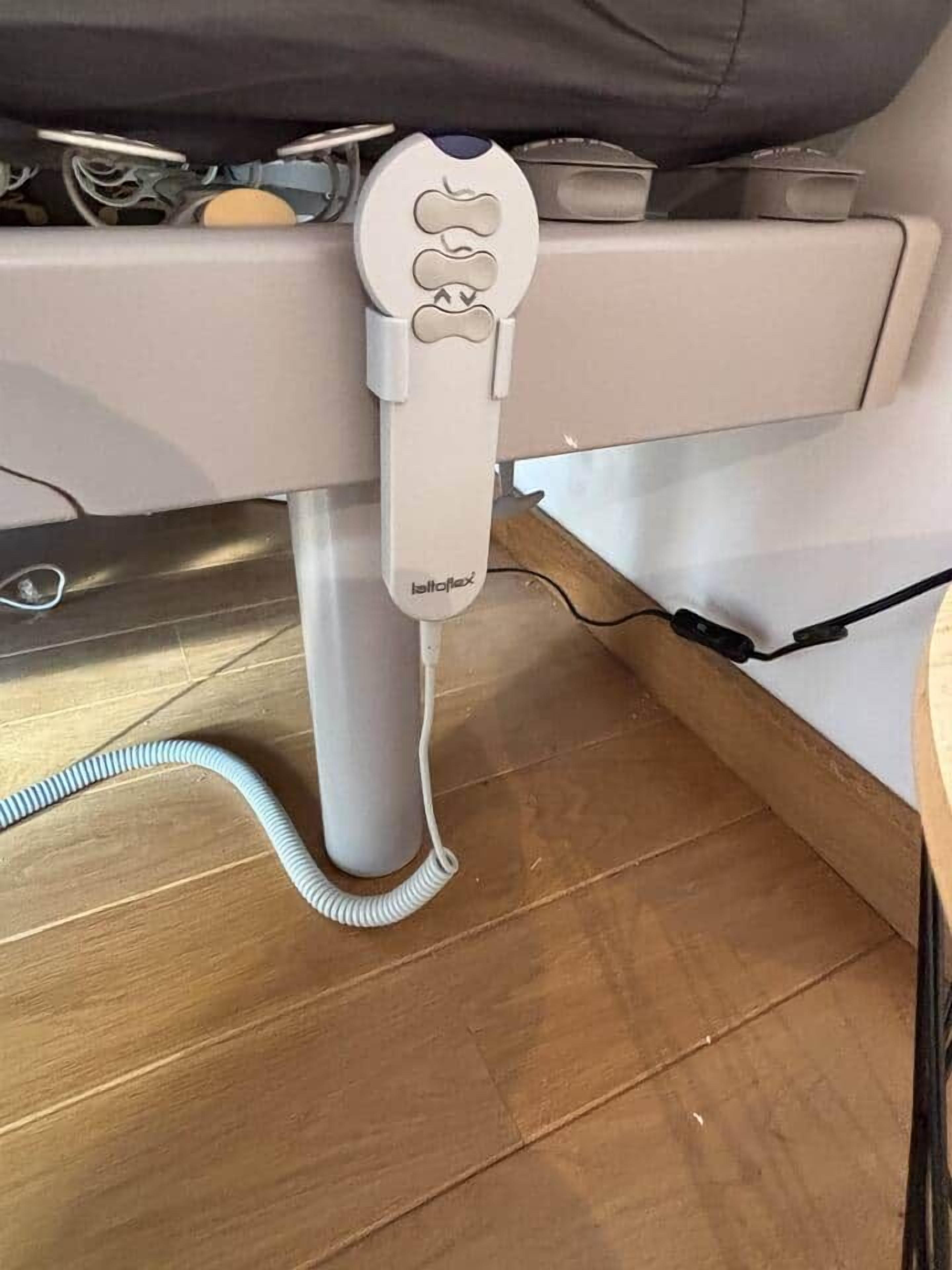 Calentador portátil blanco con cable enrollado, colocado sobre un suelo de madera junto a una cama.