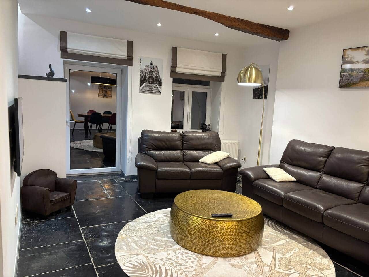 A modern living room with leather sofas, a round coffee table, and a dining area in the background.