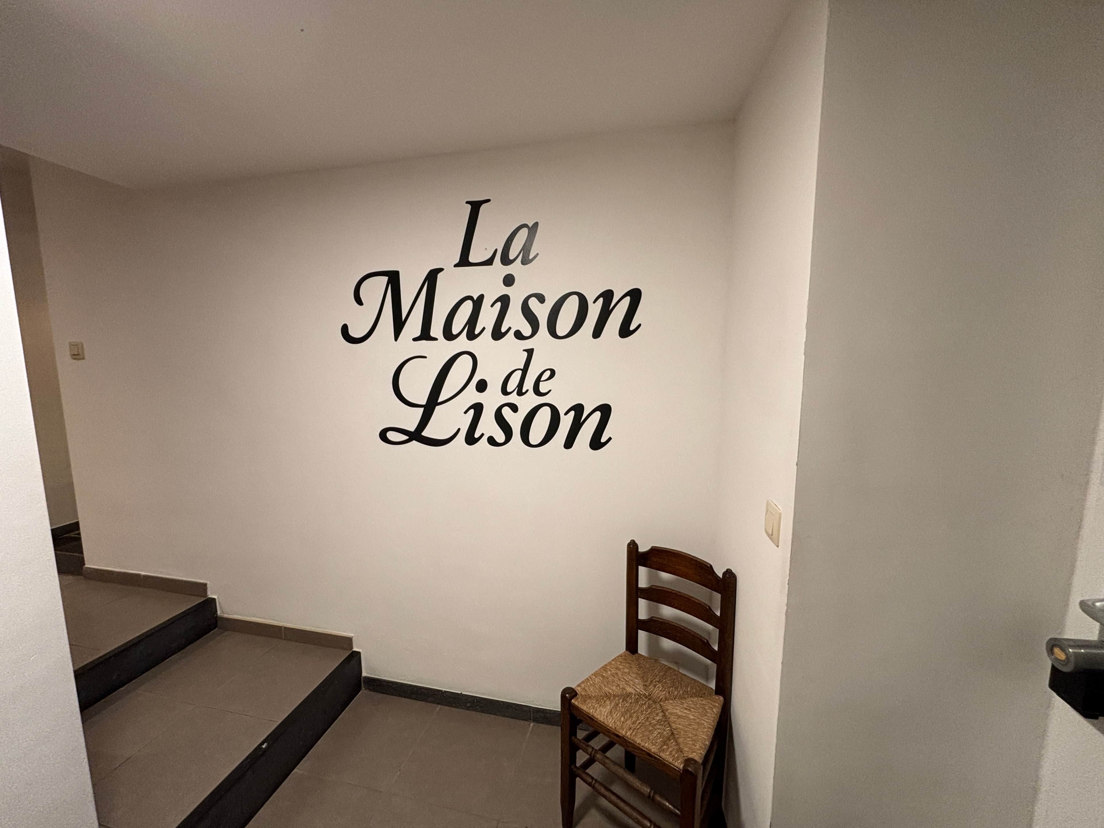 A room with a wall sign reading 'La Maison de Lison' and a wooden chair in the corner.
