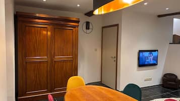 Een kamer met een houten kast, een aan de muur bevestigde televisie en een eettafel met stoelen.