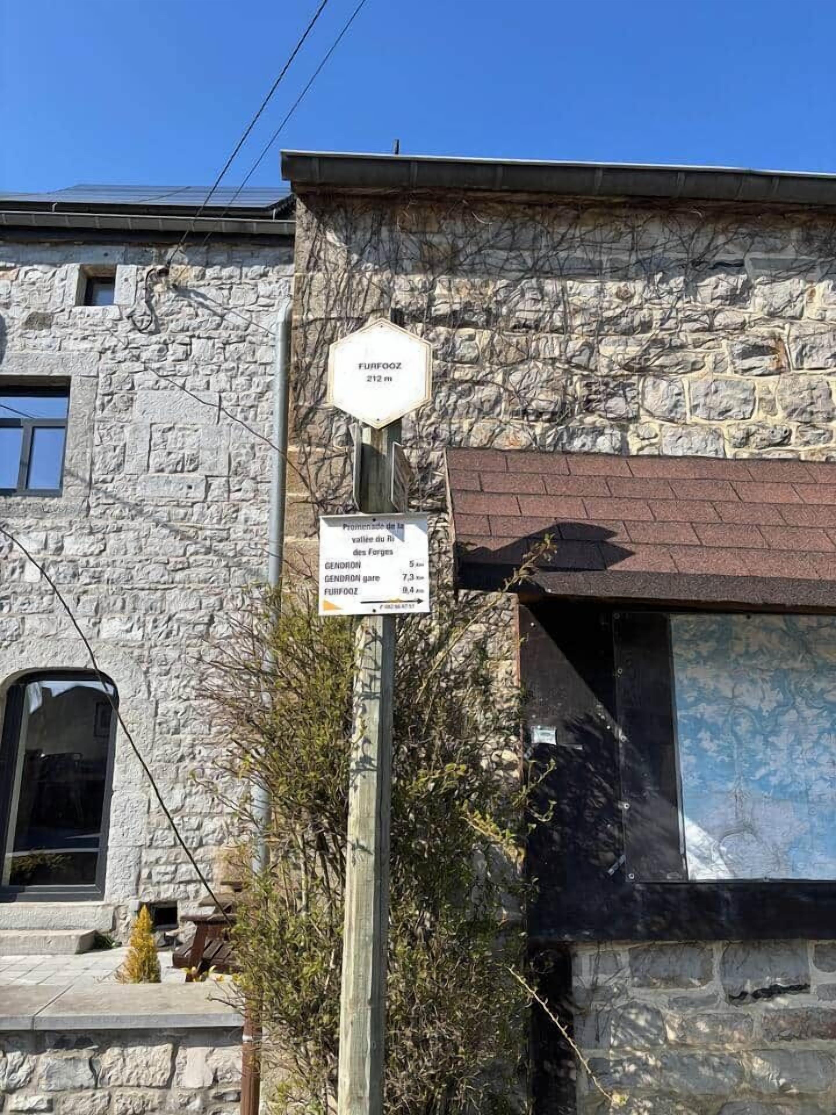 A stone building with a sign indicating 'Furfooz 212 m' and 'Promenade de la vallée du R. Gendron 5.4'.