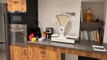 Een keuken met houten kastjes, een roestvrijstalen oven, een koffiezetapparaat, een weegschaal, en een plank met boeken en een voorraadbus.
