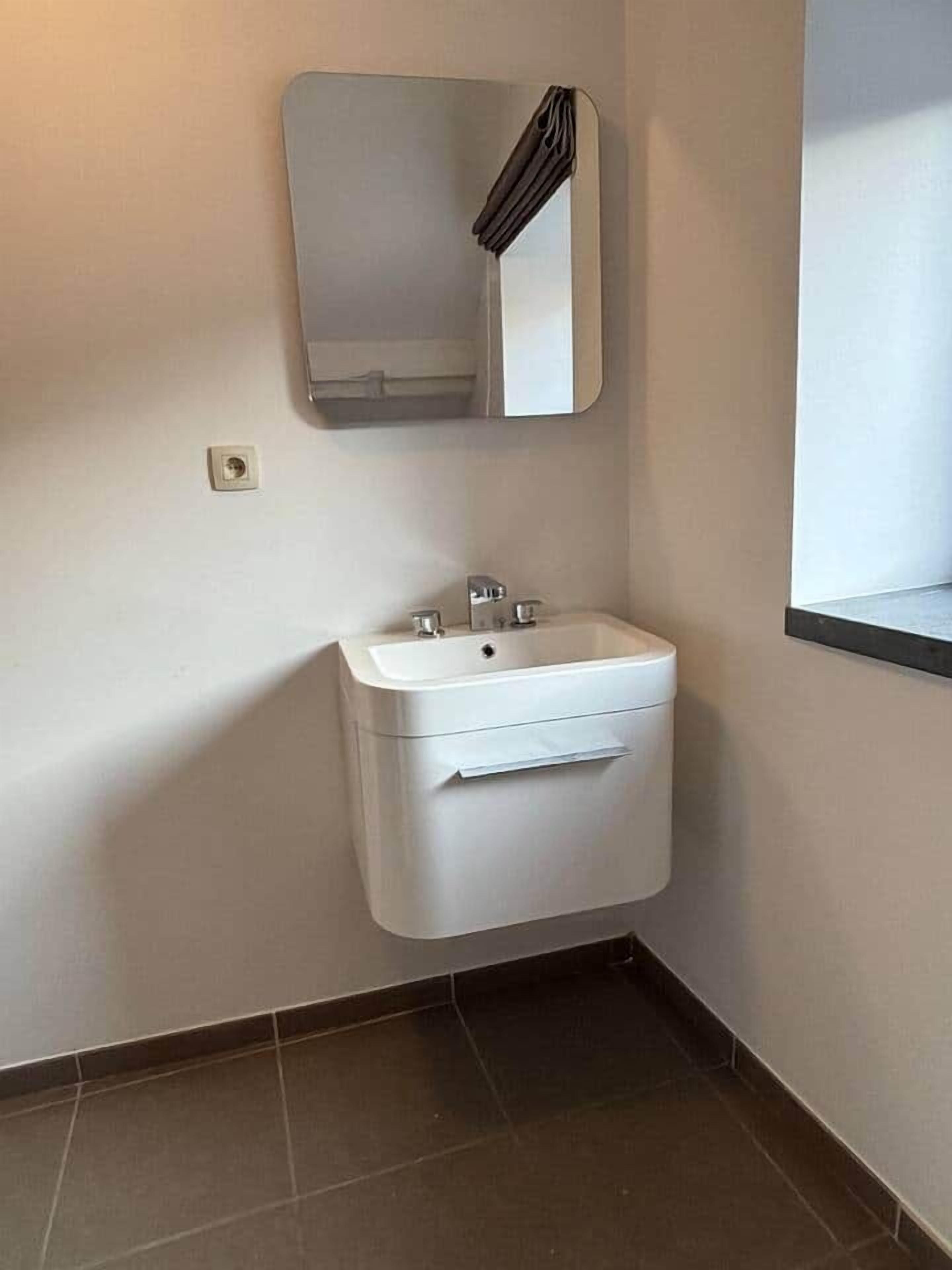 Bany d'angle amb un lavabo blanc, un mirall i una barra de tovalloles.