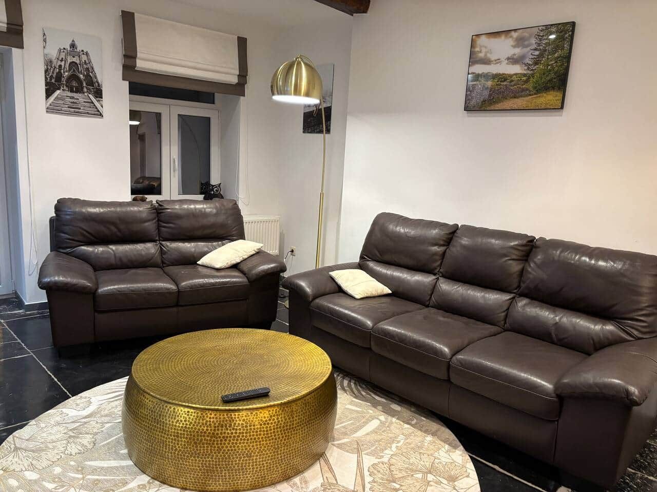 Un salon avec deux canapés en cuir marron, une table basse ronde dorée et un lampadaire.