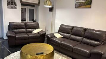 A living room with two brown leather sofas, a round gold coffee table, and a floor lamp.