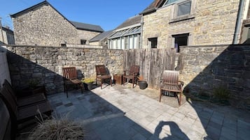 Un bâtiment en pierre doté d’un patio aménagé avec des meubles en bois et un sol en pierre.