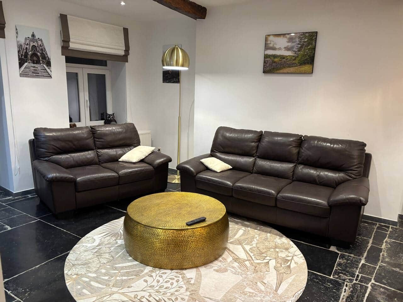Una sala de estar con dos sofás de cuero marrón oscuro, una mesa redonda con detalles dorados y una alfombra estampada.