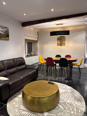 Ein modernes Wohnzimmer mit einer Ledersofa, einem runden Couchtisch und einem Essbereich mit bunten Stühlen.