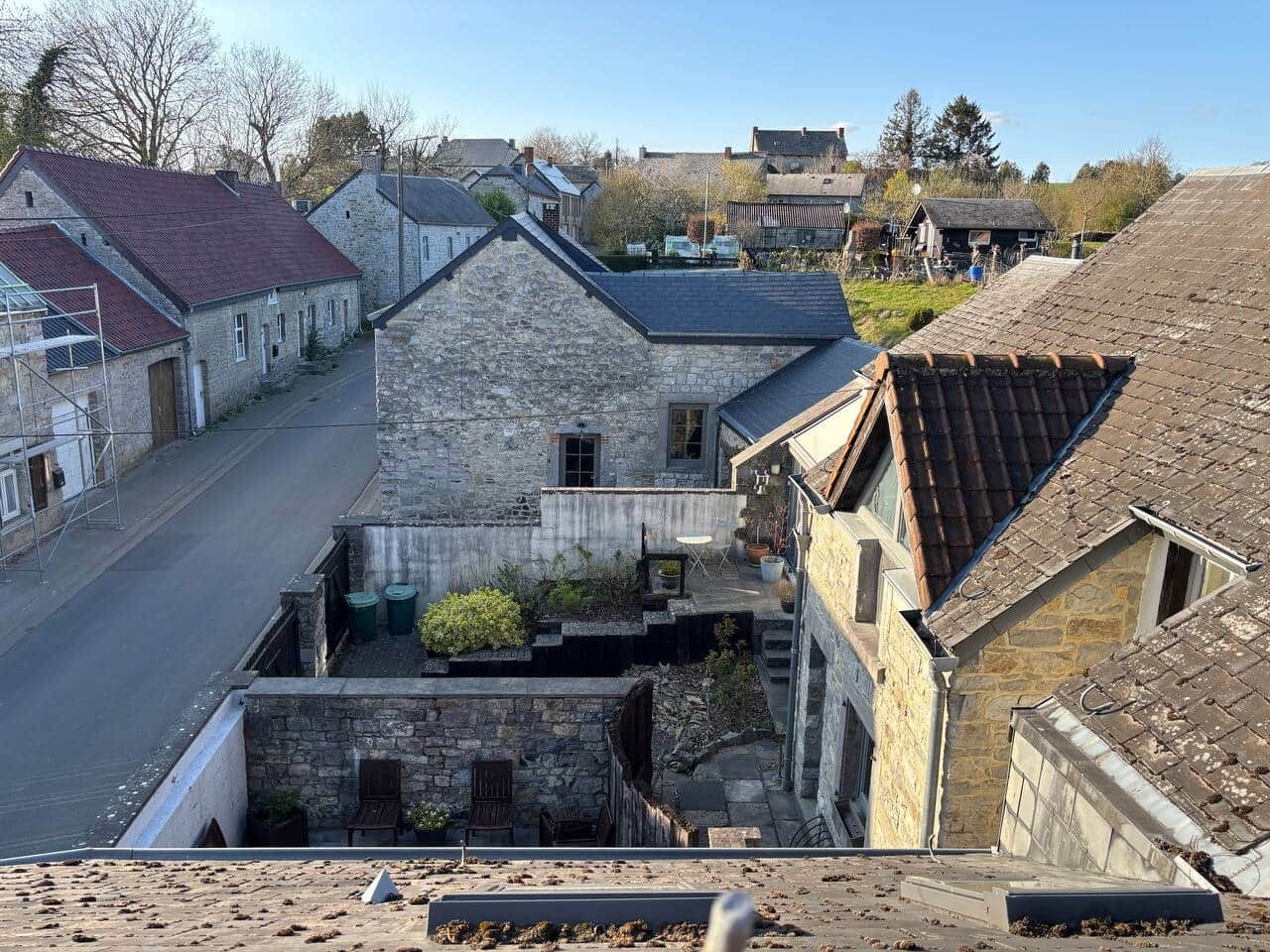A narrow street with stone buildings, a small courtyard with plants, and a clear sky.