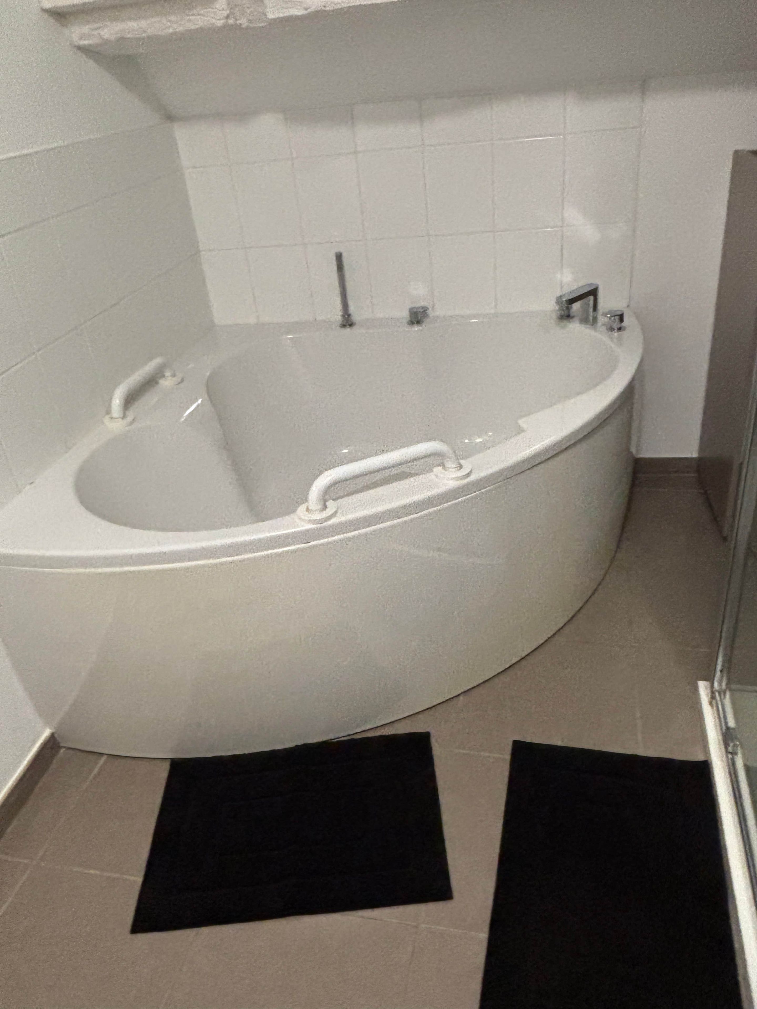 Eine große, weiße, freistehende Badewanne in einem Badezimmer mit weißen Fliesen an den Wänden und einem gefliesten Boden.