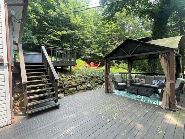 Um deck de madeira com um gazebo, área de estar externa e escadas para outro deck.