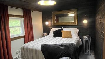 A bedroom with a bed, a mirror, a window with curtains, and a stool.