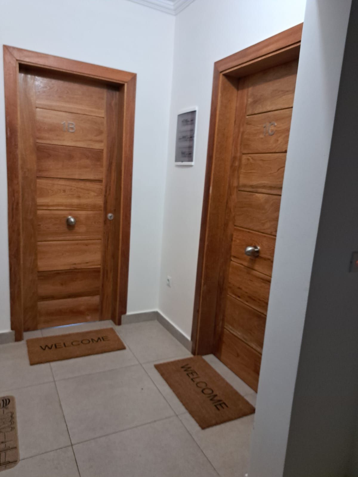 A hallway with two wooden doors, each marked with a number. There are welcome mats on the floor.