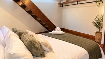 Ein Schlafzimmer mit schrägem Dach, einem Bett mit weißer Bettwäsche, einer grünen Tagesdecke und einer hängenden Pflanze.