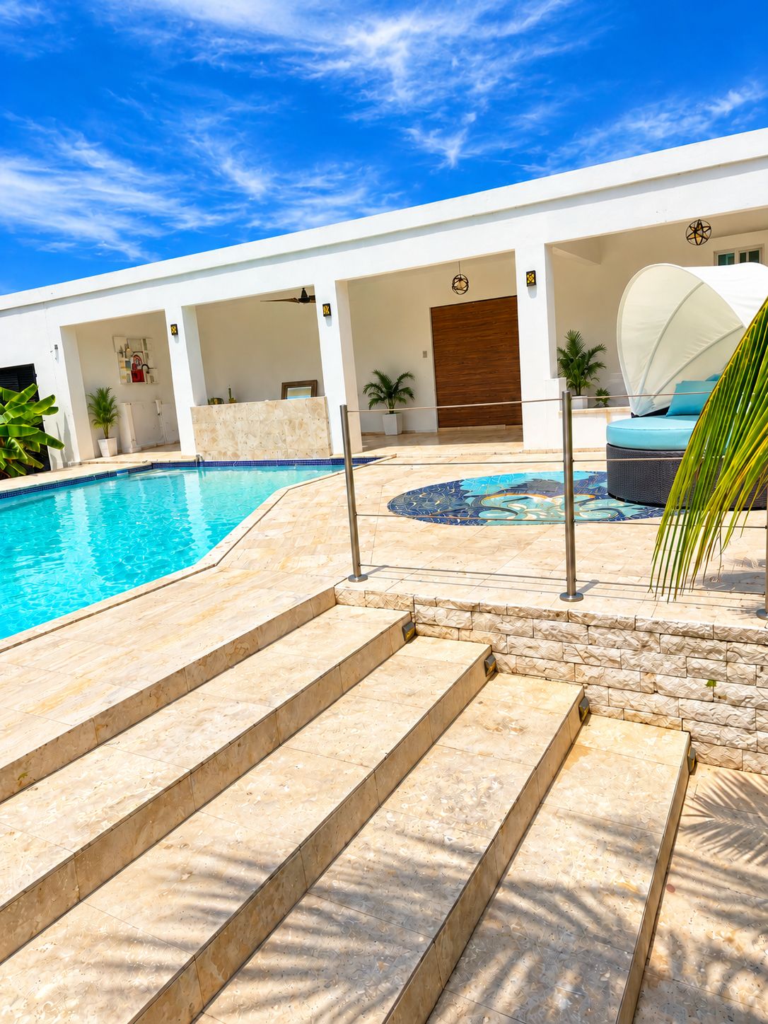 Une piscine avec des marches menant à un espace de repos couvert, entouré d’un bâtiment blanc doté d’une porte en bois.