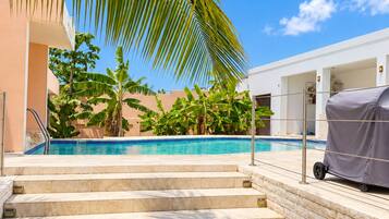 A swimming pool with steps leading down to the water, surrounded by palm trees and a building.
