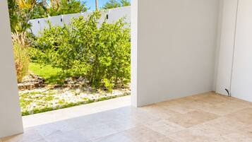 A room with a tiled floor and a view of a garden with palm trees and a white wall.