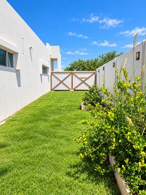 A modern building with a white exterior, a well-maintained grassy lawn, and a wooden gate. - Arecibo Pool House  2BR Tropical Escape (Islote)