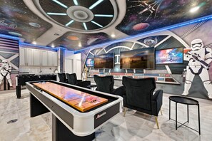 A room with a foosball table, a bar area, and Star Wars-themed decor including a large screen and a space-themed ceiling. - Luxury 15br Suites, Pool and Themed Bedrooms (Orlando)