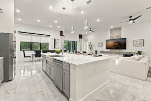 A modern kitchen with a central island, dining area, and a living space with a large TV. - Luxury 15br Suites, Pool and Themed Bedrooms (Orlando)