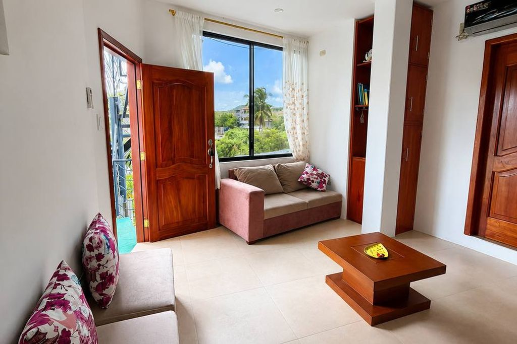 A living room with a sofa, a coffee table, a window with curtains, and a door.