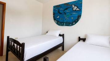 Une chambre avec deux lits simples, un tableau représentant la vie marine accroché au mur, et une porte située sur le côté gauche.