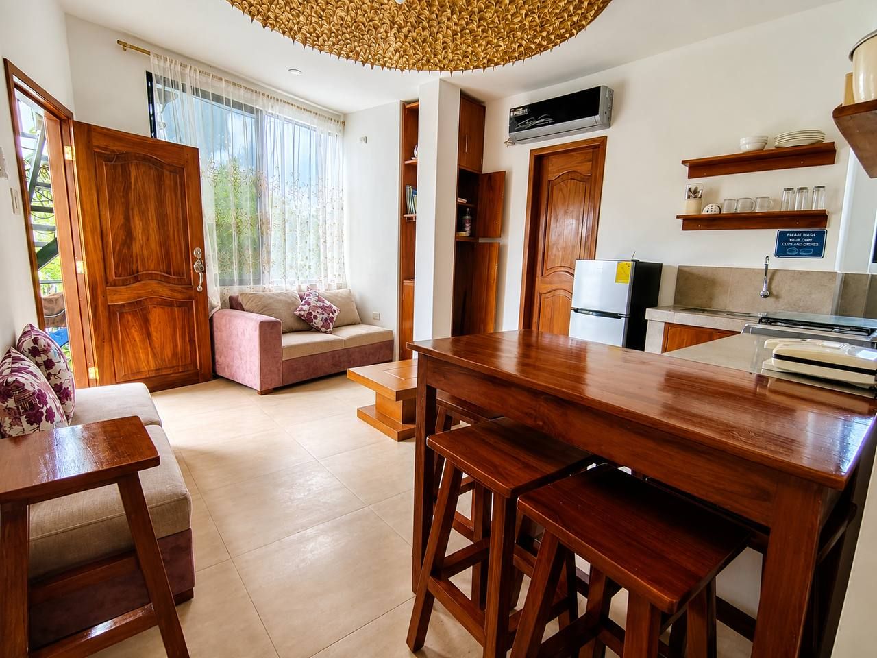Una cocina moderna con armarios de madera, un comedor con mesa y sillas de madera, un sofá y un ventanal con cortinas.