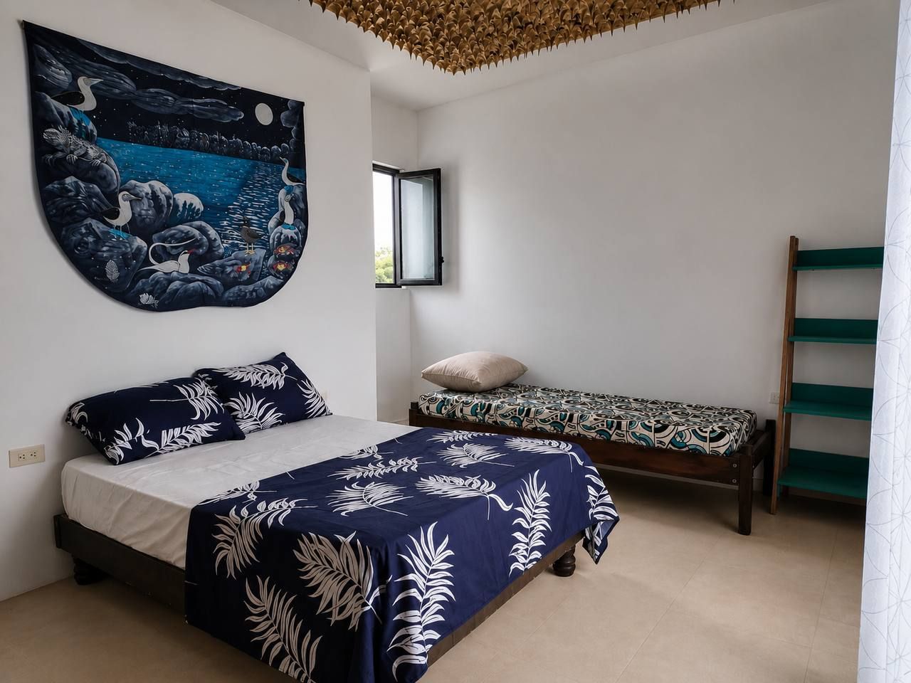 A bedroom with a bed, a smaller bed, a wall tapestry, and a shelf.