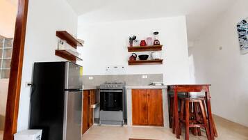 Une cuisine de taille réduite, équipée d’un réfrigérateur, d’une cuisinière et de meubles de rangement en bois.