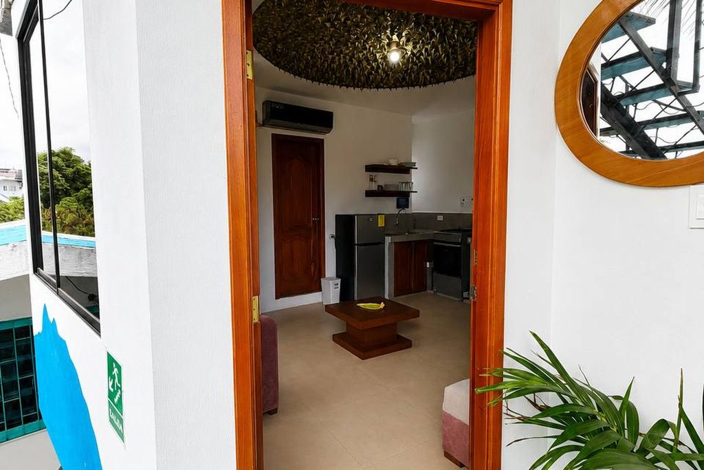 Un couloir étroit mène à une cuisine équipée d’une table et de chaises, d’un ventilateur de plafond et offrant une vue sur un bâtiment à l’extérieur.