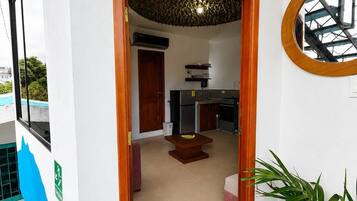 Un couloir étroit mène à une cuisine équipée d’une table et de chaises, d’un ventilateur de plafond et offrant une vue sur un bâtiment à l’extérieur.