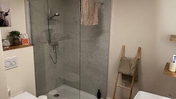 A modern bathroom with a glass-enclosed shower, a white toilet, and a wooden floor.