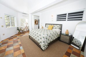 Un dormitorio con cama, mesita de noche, espejo y ventana con persianas.