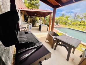 Un patio al aire libre con una parrilla, una piscina y un área de estar techada.