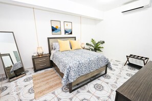 Ein Schlafzimmer mit Bett, Nachttisch, Lampe, Spiegel und einer hängenden Pflanze.